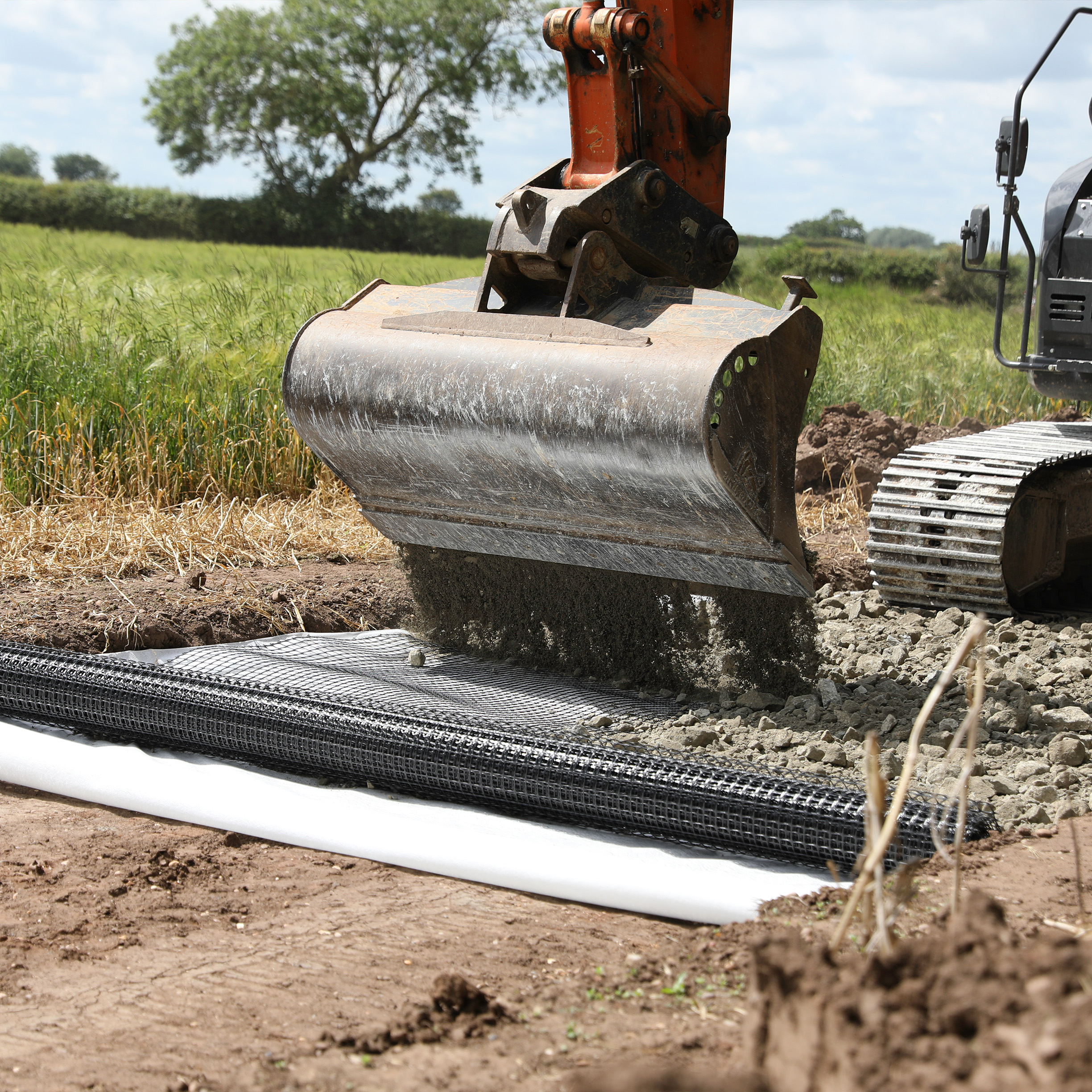 A digger pouring aggregate onto a newly laid roll of geogrid